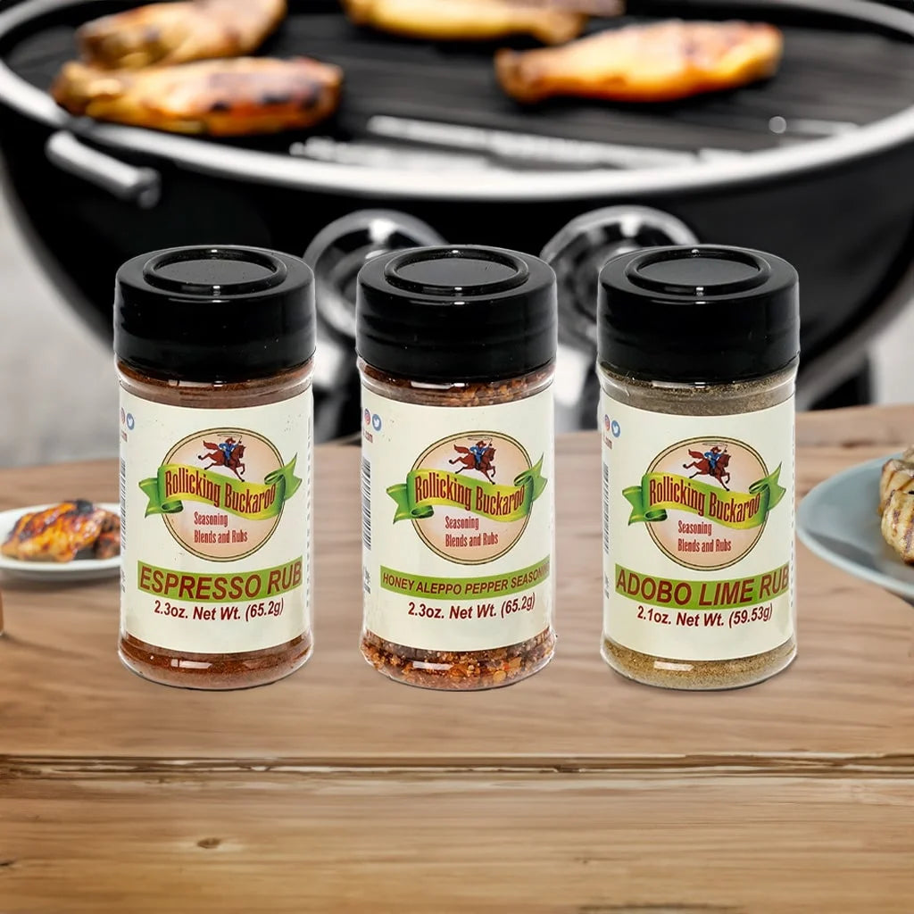 espresso rub, honey aleppo pepper seasoning, and adobe lime rub seasoning blends next to each other on a counter top and barbecue pit in the back
